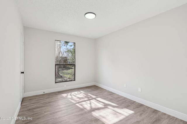 spare room featuring a textured ceiling, light wood-type flooring, and baseboards