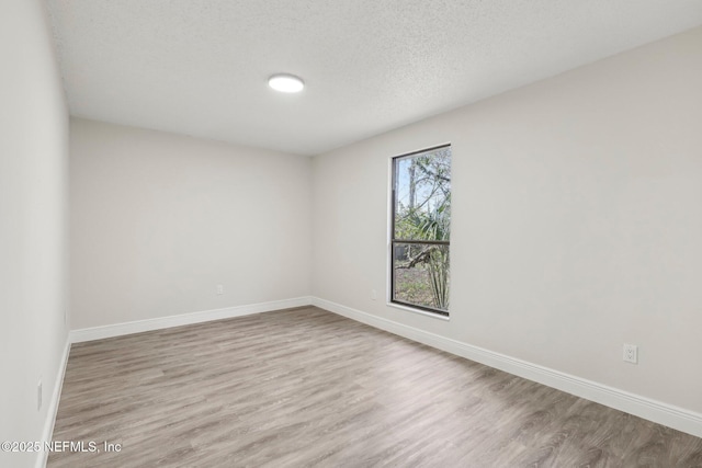 spare room featuring a textured ceiling, light wood-type flooring, and baseboards