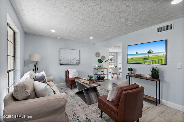 living area with baseboards, a textured ceiling, visible vents, and wood finished floors