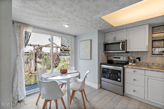 kitchen featuring stainless steel appliances, light wood-style flooring, white cabinets, a textured ceiling, and baseboards