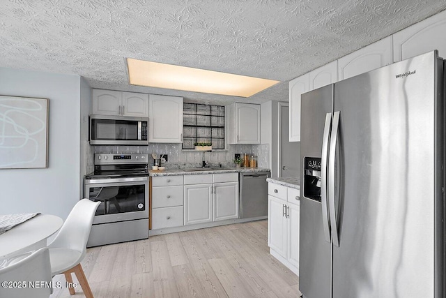 kitchen featuring tasteful backsplash, appliances with stainless steel finishes, light stone counters, light wood-style floors, and a sink