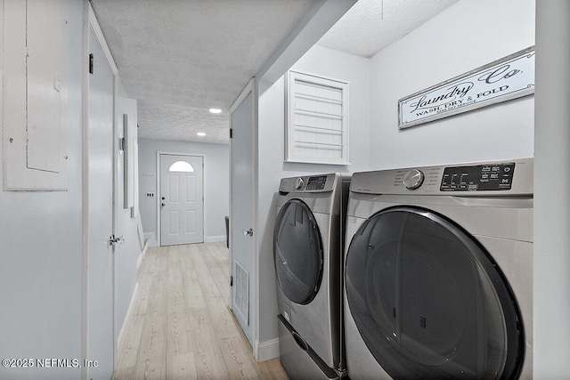 laundry room featuring light wood finished floors, a textured ceiling, washer and dryer, laundry area, and baseboards