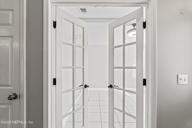 hallway featuring visible vents, a textured ceiling, and light tile patterned floors