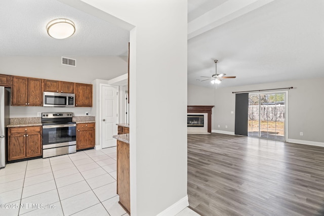 kitchen featuring stainless steel appliances, visible vents, a glass covered fireplace, vaulted ceiling, and baseboards