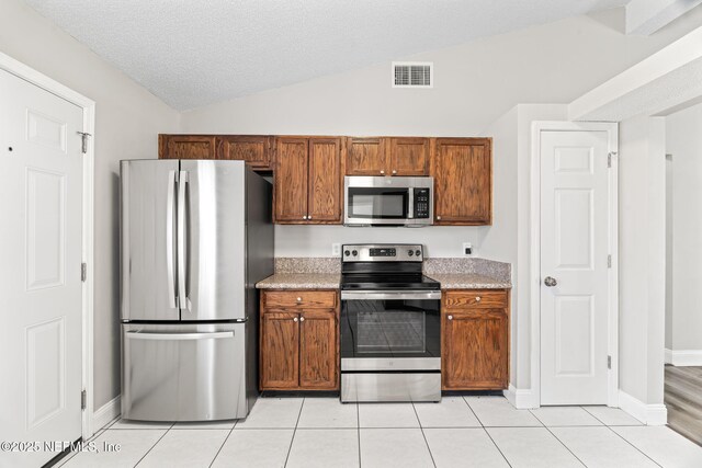 kitchen with a textured ceiling, stainless steel appliances, visible vents, vaulted ceiling, and light countertops