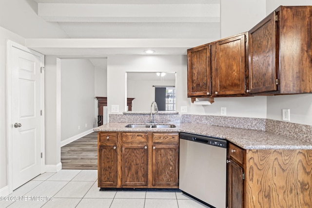 kitchen with light tile patterned floors, stainless steel dishwasher, a sink, and light stone counters