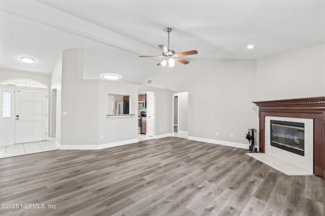 unfurnished living room featuring vaulted ceiling, wood finished floors, a fireplace with flush hearth, and baseboards