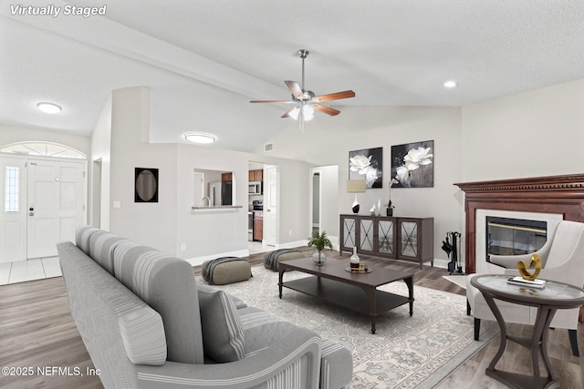 living room featuring a fireplace with flush hearth, baseboards, vaulted ceiling, and wood finished floors