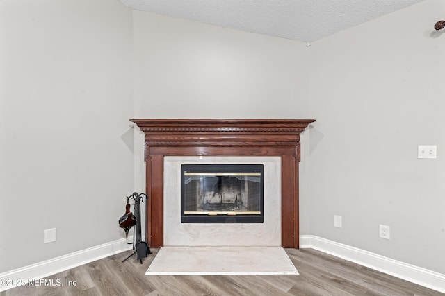 room details featuring a textured ceiling, baseboards, wood finished floors, and a glass covered fireplace