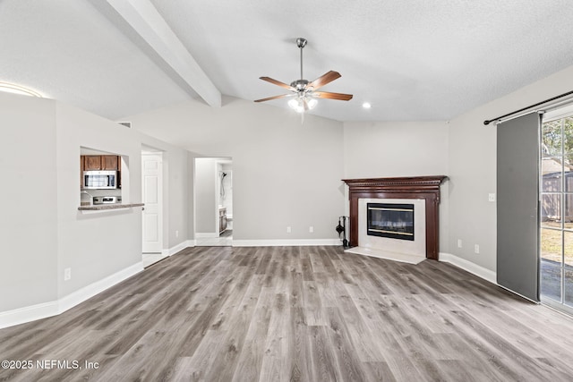 unfurnished living room with a fireplace with flush hearth, lofted ceiling with beams, baseboards, and wood finished floors