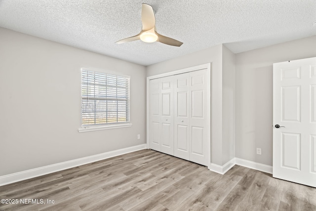 unfurnished bedroom with a closet, ceiling fan, a textured ceiling, wood finished floors, and baseboards