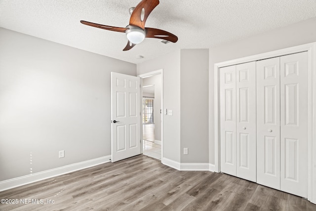 unfurnished bedroom with a textured ceiling, a closet, wood finished floors, and baseboards