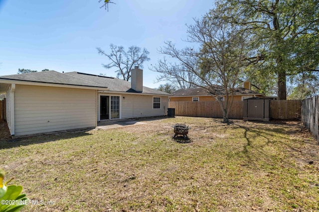 rear view of house with an outbuilding, a storage unit, a lawn, a fenced backyard, and a fire pit