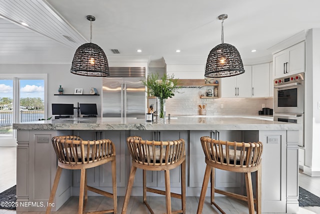 kitchen featuring open shelves, a spacious island, appliances with stainless steel finishes, white cabinets, and light stone countertops