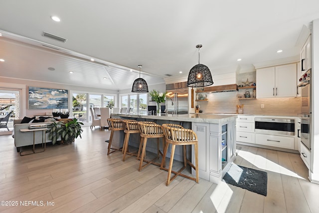 kitchen featuring visible vents, white cabinetry, appliances with stainless steel finishes, open shelves, and an island with sink