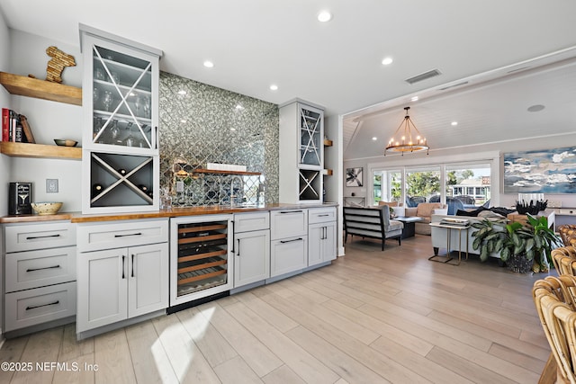 bar with beverage cooler, visible vents, an inviting chandelier, light wood-type flooring, and pendant lighting