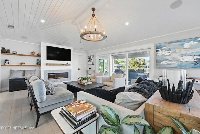 living room featuring light wood-style flooring, a glass covered fireplace, lofted ceiling with beams, and an inviting chandelier