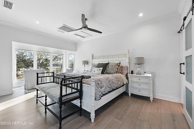 bedroom featuring a barn door, baseboards, visible vents, dark wood-style floors, and crown molding