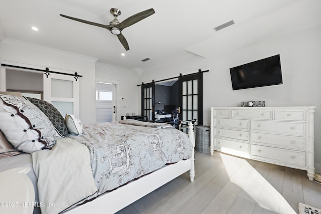 bedroom featuring light wood-style floors, visible vents, ornamental molding, and a barn door