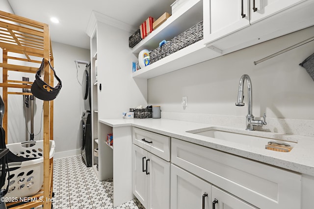 laundry room featuring cabinet space, baseboards, stacked washer / dryer, light floors, and a sink