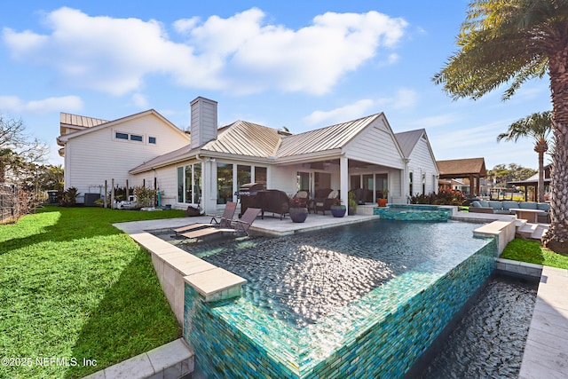 back of house with a chimney, metal roof, a standing seam roof, a yard, and a patio area