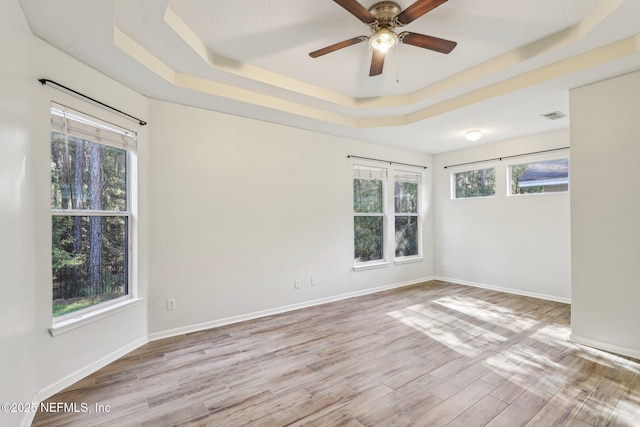 empty room with visible vents, a tray ceiling, light wood-type flooring, and a wealth of natural light