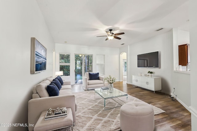 living area with arched walkways, wood finished floors, visible vents, baseboards, and a ceiling fan