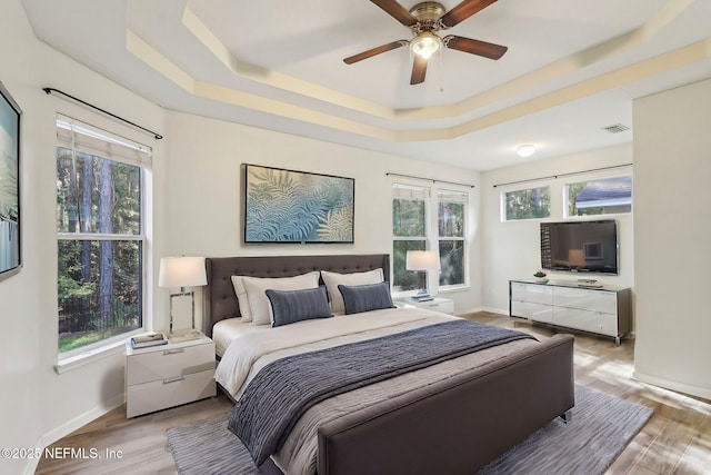 bedroom featuring light wood-style flooring, multiple windows, a raised ceiling, and visible vents