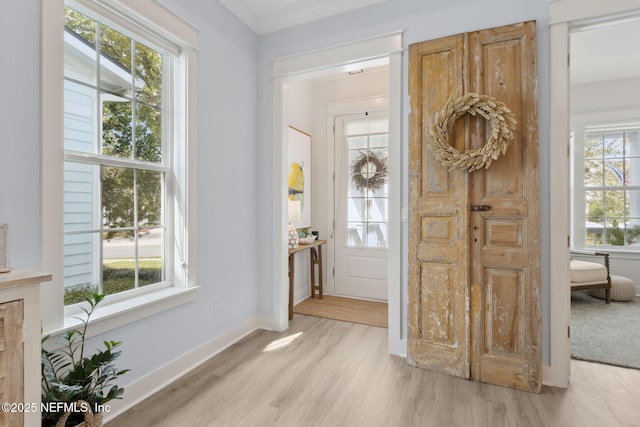 foyer entrance with baseboards, a healthy amount of sunlight, crown molding, and light wood finished floors