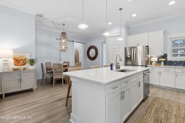 kitchen with pendant lighting, a center island with sink, stainless steel appliances, white cabinets, and a sink