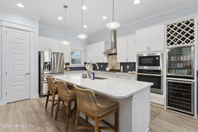 kitchen with wine cooler, stainless steel appliances, hanging light fixtures, wall chimney range hood, and light countertops