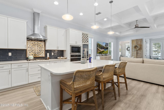 kitchen with an island with sink, wall chimney exhaust hood, open floor plan, light countertops, and white cabinetry