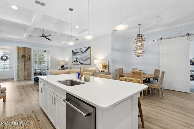 kitchen with a barn door, open floor plan, hanging light fixtures, white cabinetry, and stainless steel dishwasher