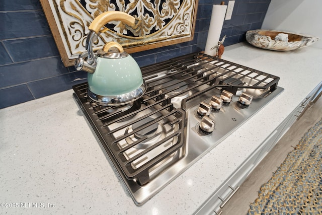 room details with light stone countertops, stainless steel gas cooktop, and backsplash