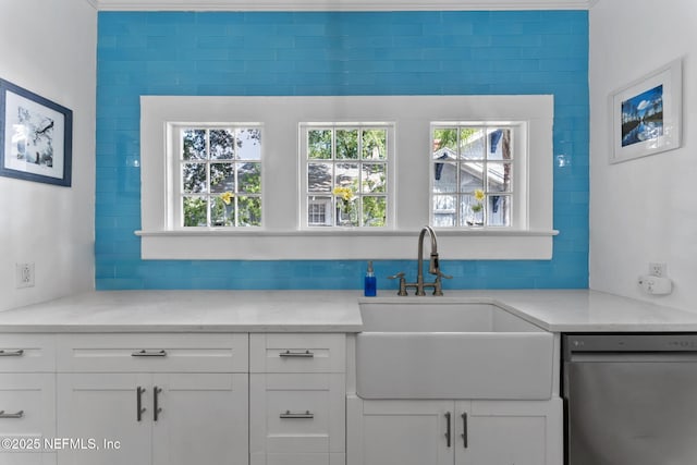 kitchen with light stone countertops, dishwasher, white cabinets, and a sink