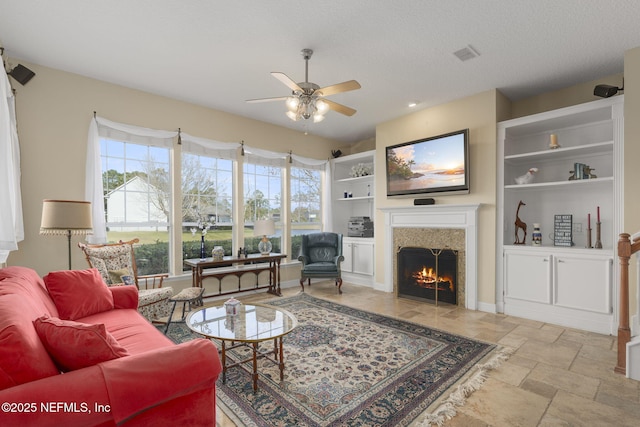 living room with visible vents, a warm lit fireplace, ceiling fan, stone tile flooring, and a textured ceiling