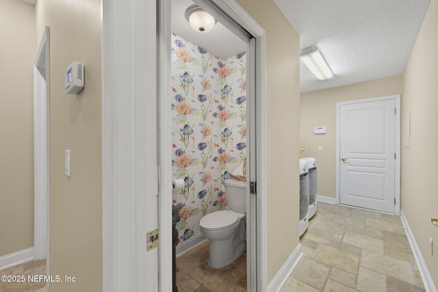 full bathroom featuring stone tile floors, toilet, baseboards, and a textured ceiling