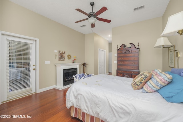 bedroom featuring a glass covered fireplace, wood finished floors, visible vents, and baseboards