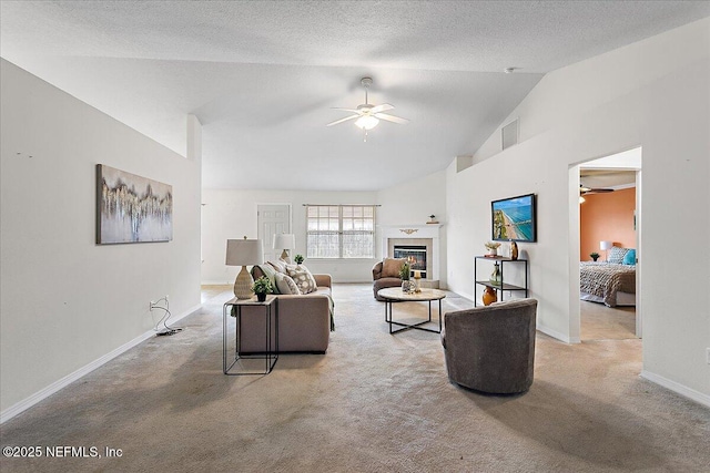 living area with visible vents, a ceiling fan, a glass covered fireplace, a textured ceiling, and carpet floors