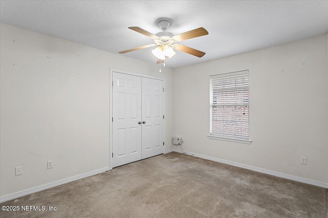 unfurnished bedroom featuring a closet, a ceiling fan, carpet flooring, a textured ceiling, and baseboards