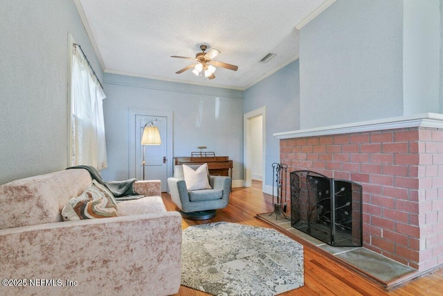 living area featuring a fireplace, crown molding, visible vents, a ceiling fan, and wood finished floors