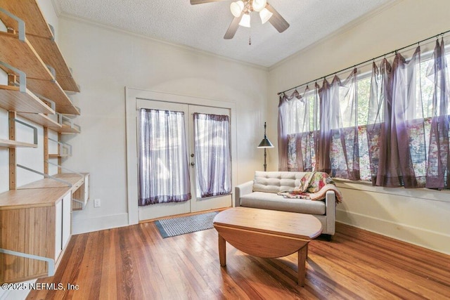 living area with a textured ceiling, wood finished floors, a ceiling fan, and crown molding