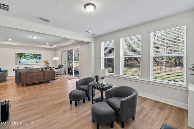 living area with visible vents, plenty of natural light, a textured ceiling, and light wood finished floors