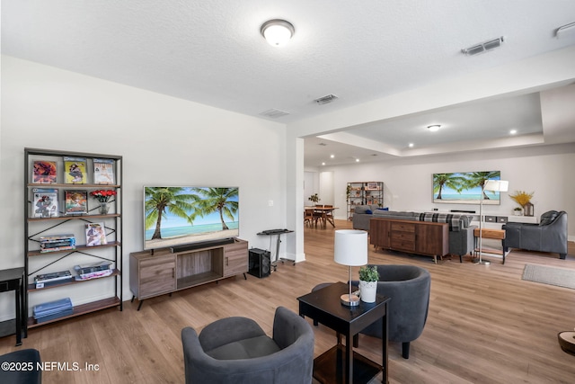 living room with a tray ceiling, a textured ceiling, visible vents, and wood finished floors