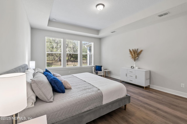 bedroom featuring a textured ceiling, wood finished floors, visible vents, baseboards, and a raised ceiling