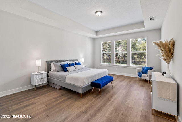 bedroom with baseboards, visible vents, a raised ceiling, wood finished floors, and a textured ceiling