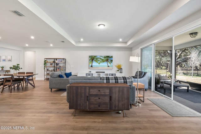 living area with light wood-style floors, a tray ceiling, visible vents, and recessed lighting