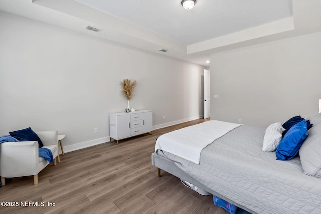 bedroom featuring baseboards, visible vents, a tray ceiling, and wood finished floors