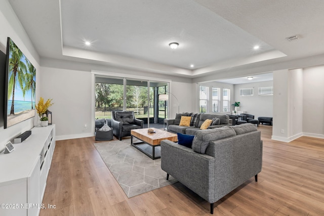 living area featuring recessed lighting, visible vents, baseboards, light wood-style floors, and a tray ceiling