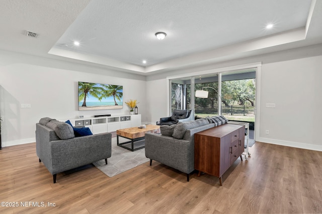 living room featuring baseboards, visible vents, a tray ceiling, a textured ceiling, and light wood-style floors